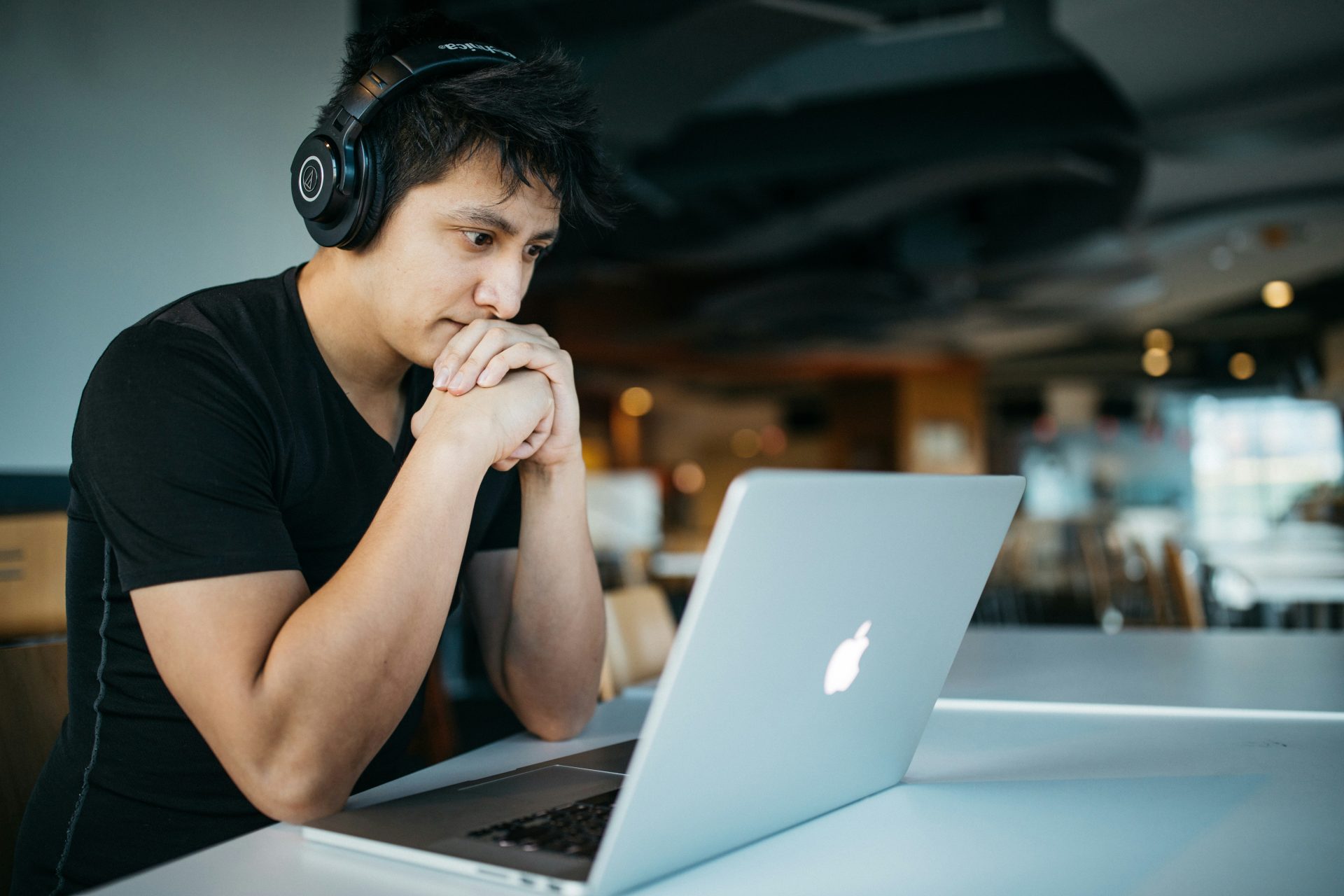 un homme portant des écouteurs assis sur une chaise devant un MacBook